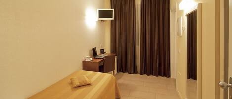 A hotel room with a bed, a desk with a computer, a TV, and curtains.