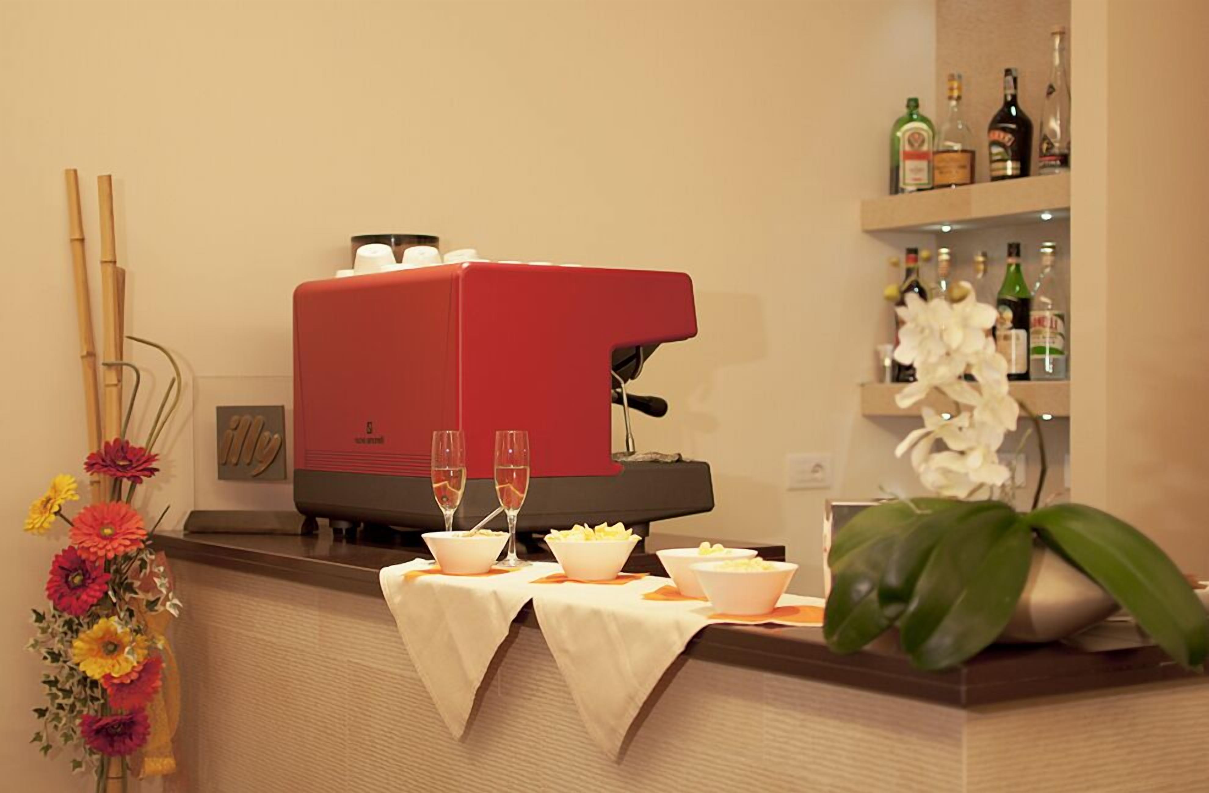 A bar area with a red espresso machine, two glasses of champagne, and a variety of bottles on shelves.