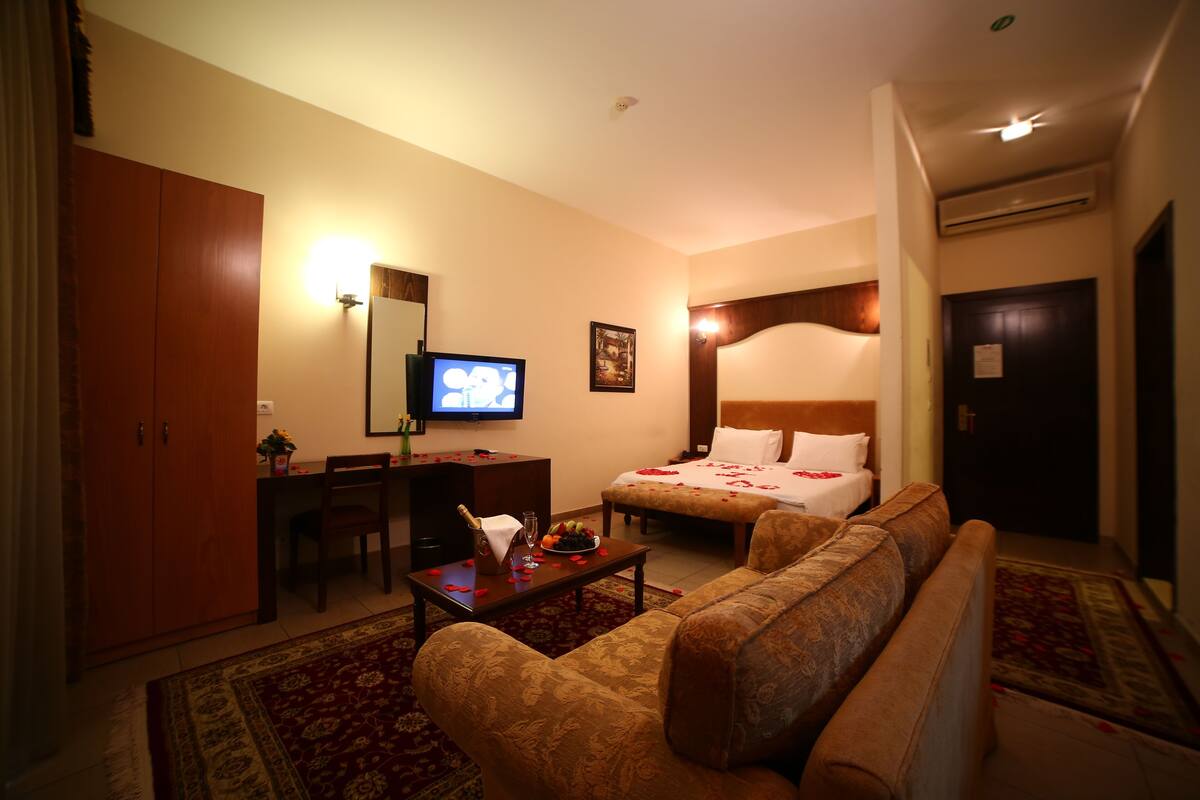 A hotel room with a bed, a sofa, a desk, a television, and a large mirror.