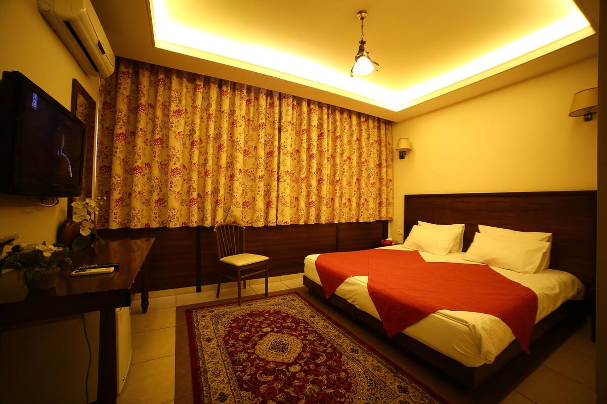 A hotel room with a bed, a desk, a chair, a TV, and a ceiling light.
