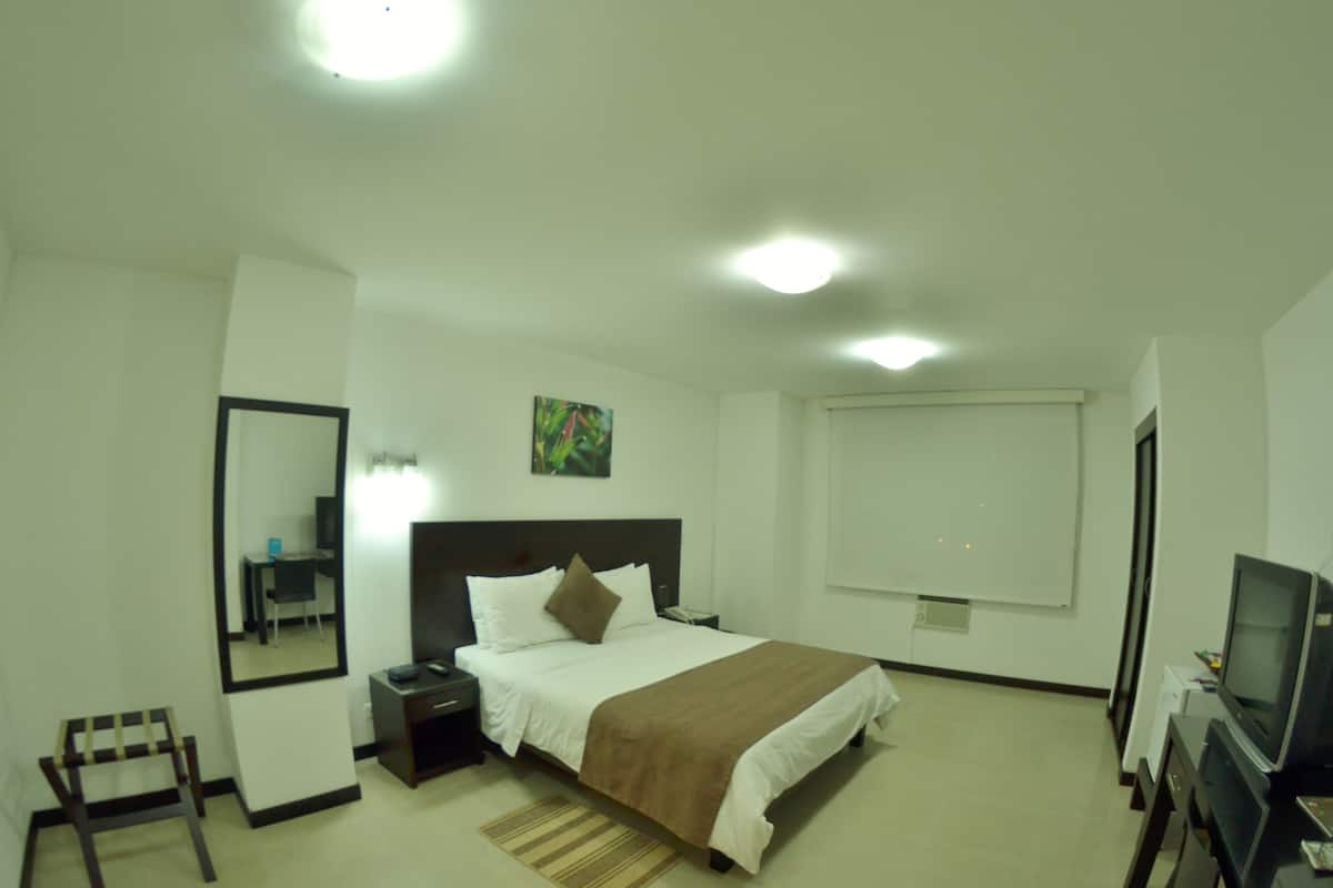 A hotel room with a bed, bedside table, chair, desk, TV, and a window.