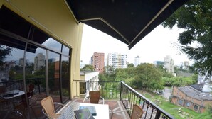 Ein Balkon mit Tisch und Stühlen, eine gelbe Wand und Blick auf eine Stadtlandschaft.