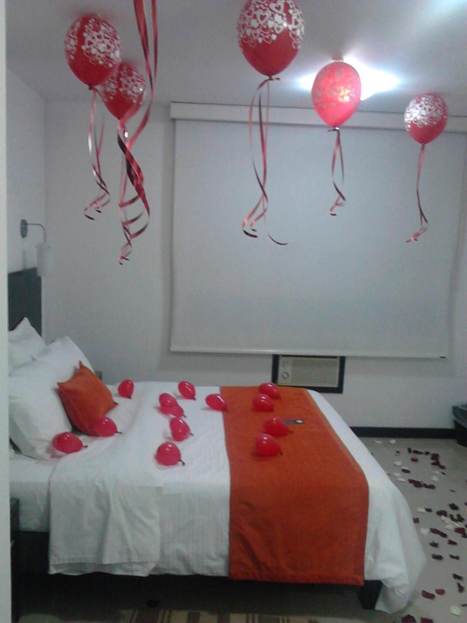 Une chambre d’hôtel avec un lit, des oreillers et une couverture. Il y a des ballons et des confettis sur le lit.