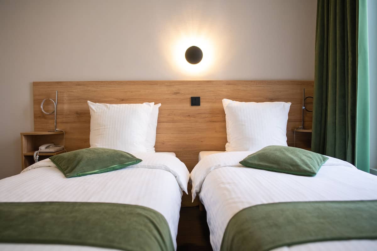 Ein Hotelzimmer mit zwei Betten, einem hölzernen Kopfteil, einem Nachttisch mit Telefon und einer Wandleuchte.