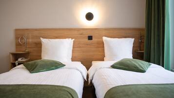 Une chambre d’hôtel avec deux lits, une tête de lit en bois, une table de chevet avec un téléphone et un luminaire fixé au mur.