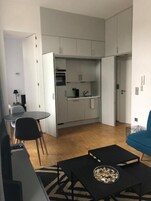 Un espacio habitable compacto con kitchenette, una zona de comedor con una mesa redonda y sillas, y un sofá.