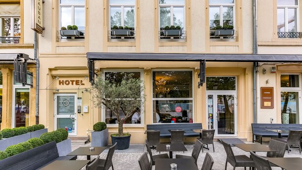 Exterior de un hotel con mesas al aire libre, un árbol y un cartel que dice "HOTEL VAUBAN".