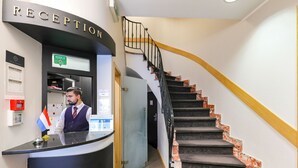 Zona de recepción con un mostrador curvo, un letrero que dice "RECEPTION" y una escalera con barandilla de madera y pasamanos negro.