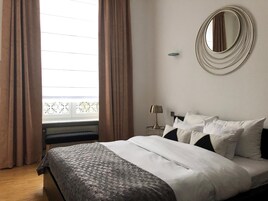 Una cama bien hecha con una colcha estampada, una lámpara de noche y un espejo redondo en la pared.
