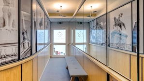 Un pasillo con obras de arte enmarcadas en las paredes, un banco y vistas al exterior a través de amplias ventanas.