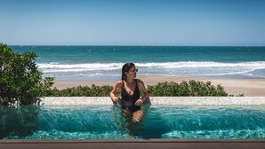 A person in a swimming pool with a beach and ocean view.