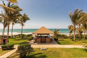 Eine Strandbar mit Holzdach, umgeben von Palmen und Blick aufs Meer.