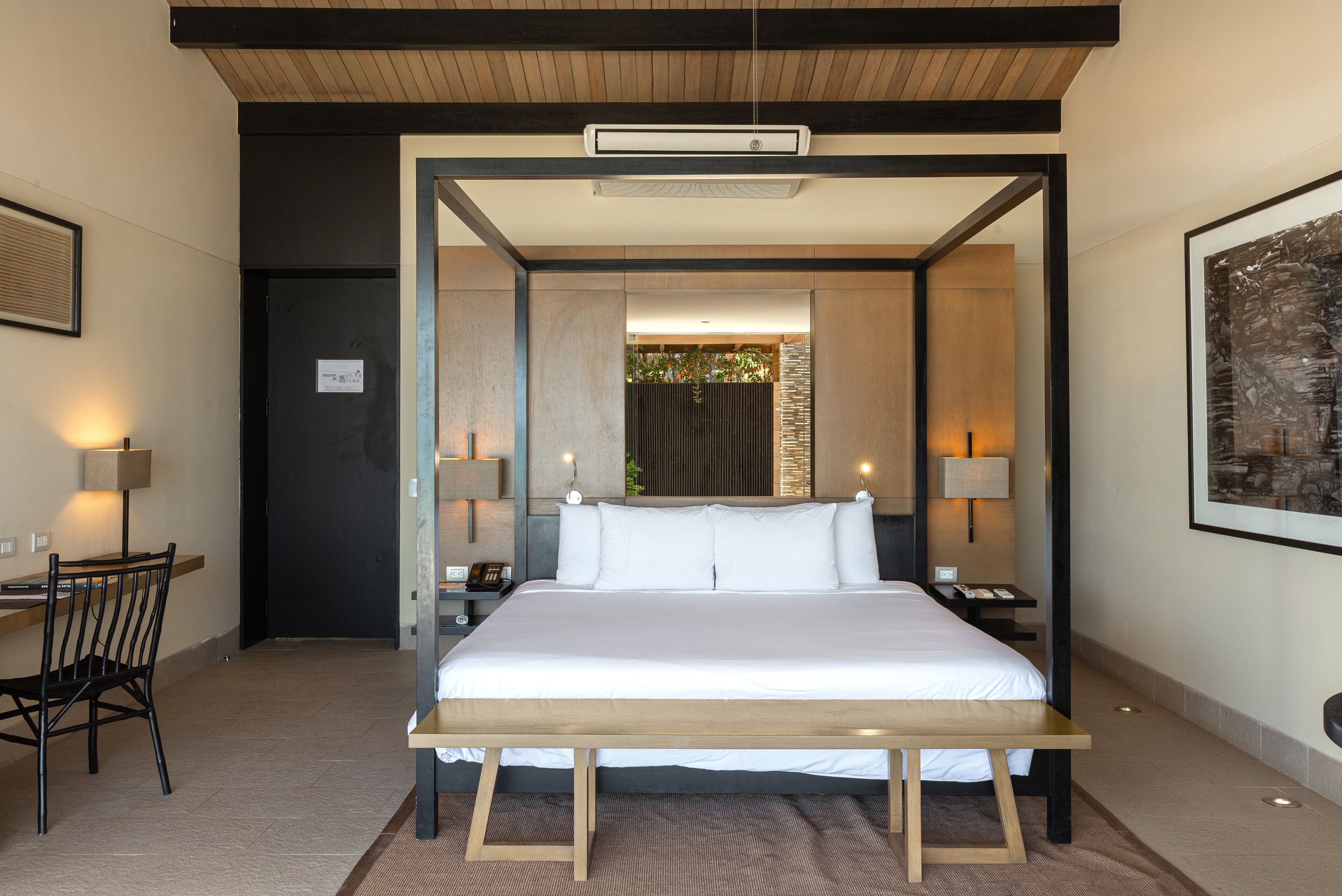 Una habitación de hotel moderna con una cama grande, mesitas de noche con lámparas, un escritorio con una silla y un cuadro en la pared.