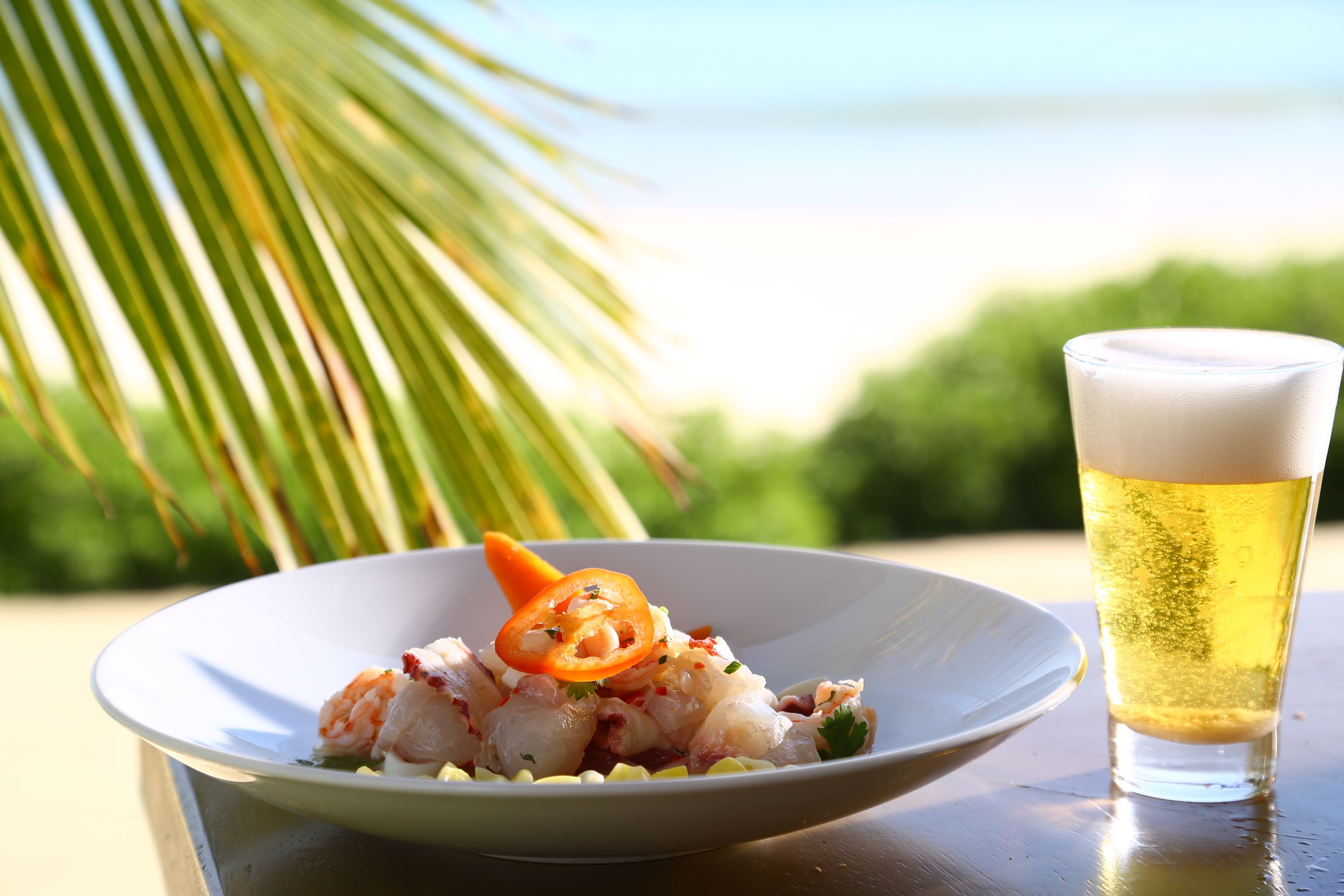 Ein Teller mit Meeresfrüchten und ein Bierglas auf einem Tisch mit Meerblick.