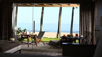 Una habitación con un gran ventanal corredera que da a una vista de la playa, un comedor con mesa y sillas, y una cama con vistas.