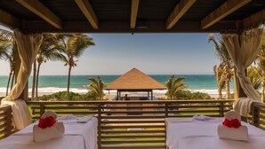A beachside hotel room with a wooden deck, two beds, and a view of the ocean.
