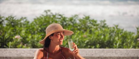 A person relaxing by a pool with a drink, surrounded by greenery.