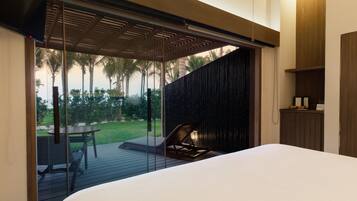 Un dormitorio moderno con una cama grande, un ventanal que da a un patio con mesa y sillas, y vistas a palmeras.