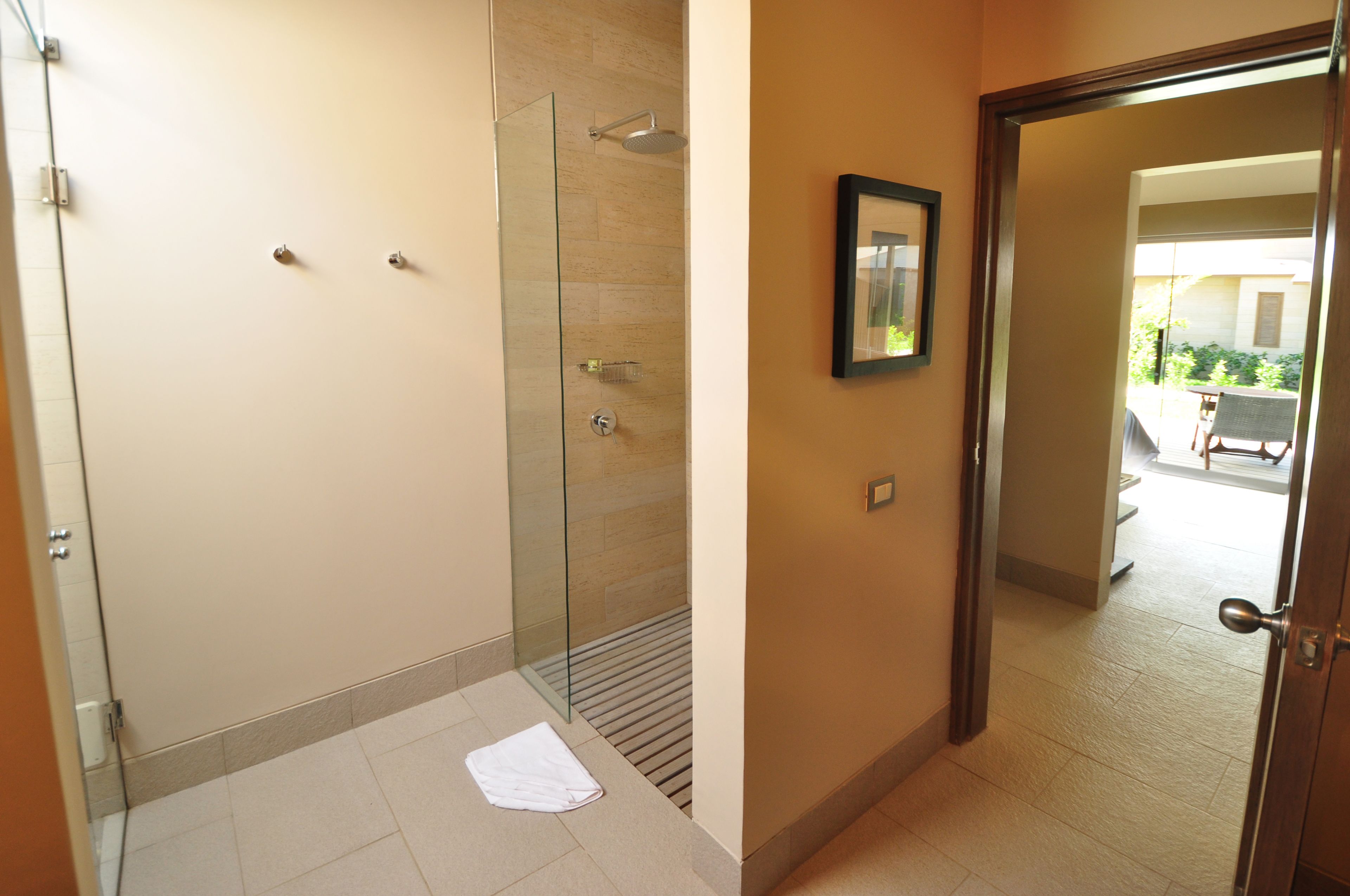 Ein modernes Badezimmer mit einer Glaskabine zur Dusche, einem weißen Handtuch auf dem Boden und einer Tür zu einem Außenbereich.