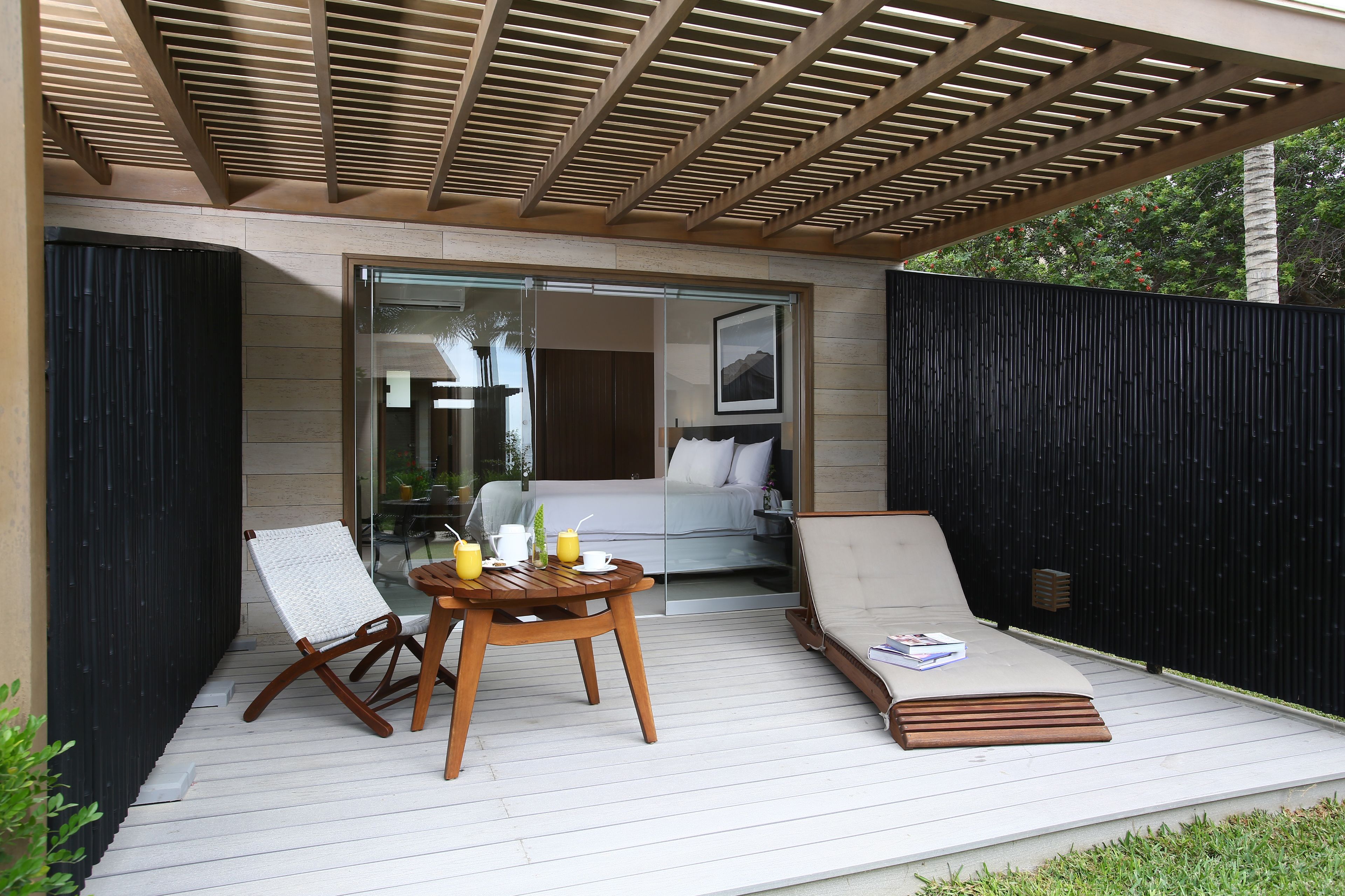 Une terrasse dotée d’une table en bois, de deux chaises longues et d’une porte vitrée donnant accès à une chambre.