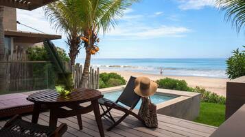Una terraza de madera con piscina, sillas de descanso y vistas a la playa y al océano.