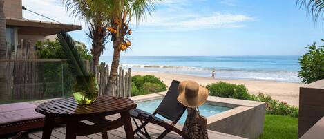 Una terraza de madera con piscina, sillas de descanso y vistas a la playa y al océano.