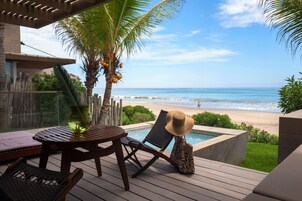 Una terraza de madera con piscina, sillas de descanso y vistas a la playa y al océano.