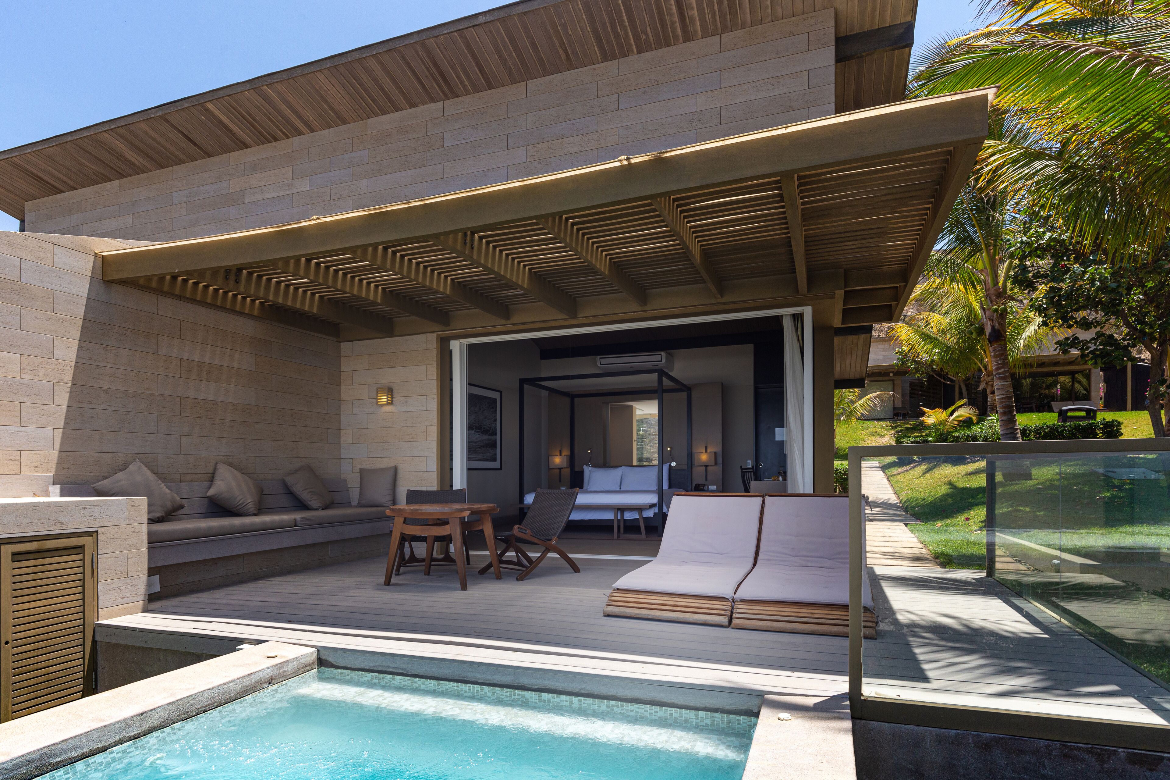 Un área de piscina exterior moderna con cubierta de madera, asientos y un espacio con paredes de vidrio.