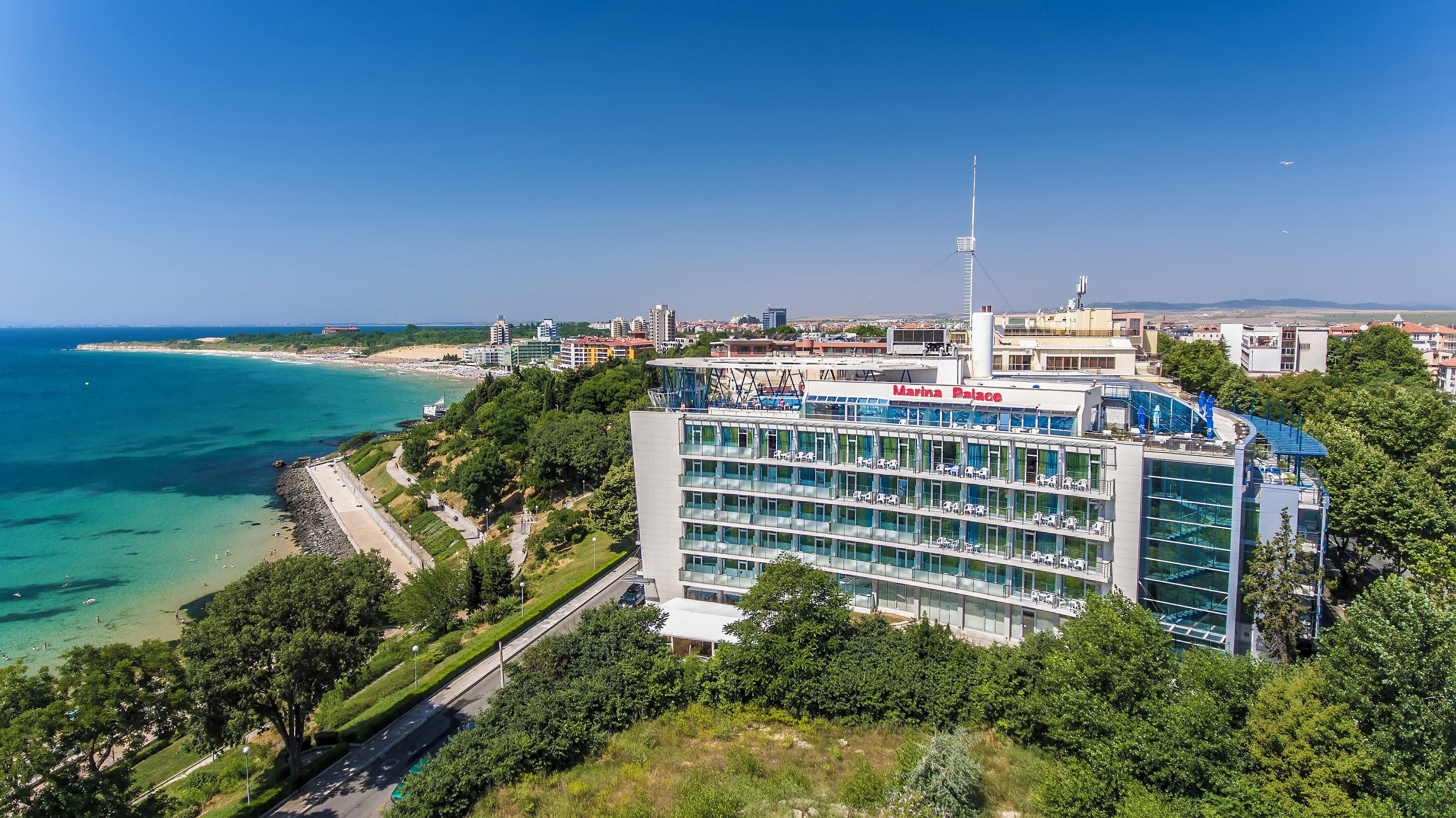 A modern building with a marina palace sign, surrounded by greenery and a beach.