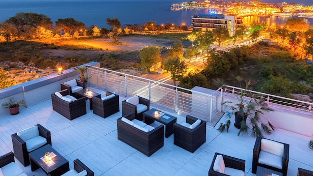 Une terrasse sur le toit, aménagée avec des meubles en osier et des plantes en pot, offrant une vue sur le paysage urbain et la mer.