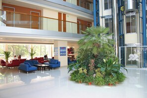 Un hall d’entrée spacieux, doté de plusieurs espaces de détente, d’un arrangement floral central et d’une rambarde en verre donnant sur le niveau inférieur.