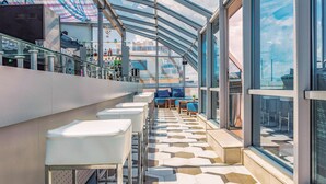 Un espace bar moderne doté de rampes de protection en verre, de sièges et d’un sol à motifs.