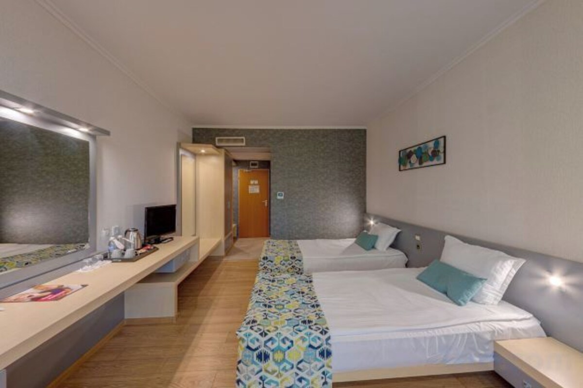 Habitación de hotel con cama, mesita de noche y un espejo. Se ve una puerta que da a un pasillo.