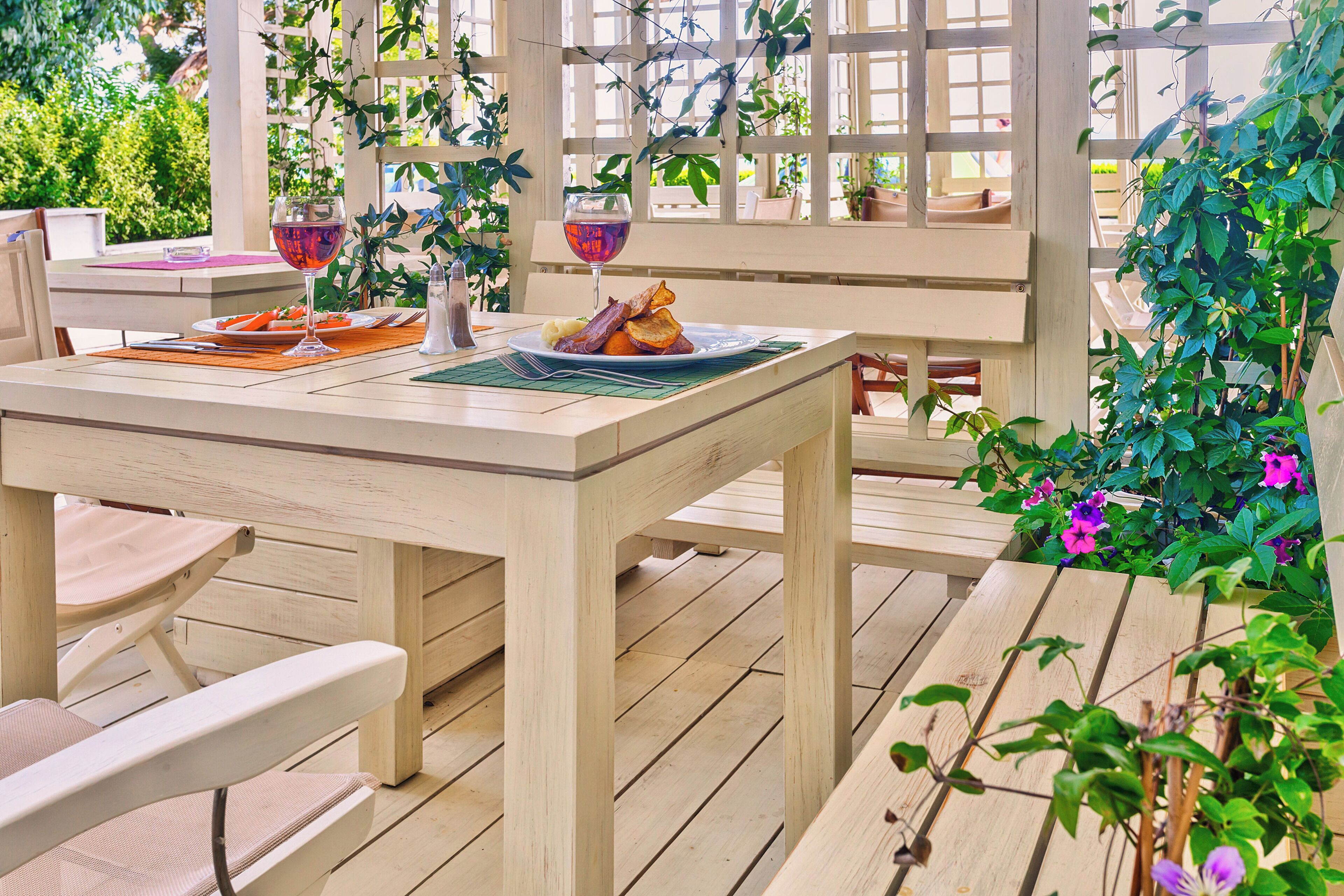 An outdoor wooden deck with a table set for a meal, surrounded by chairs and potted plants.