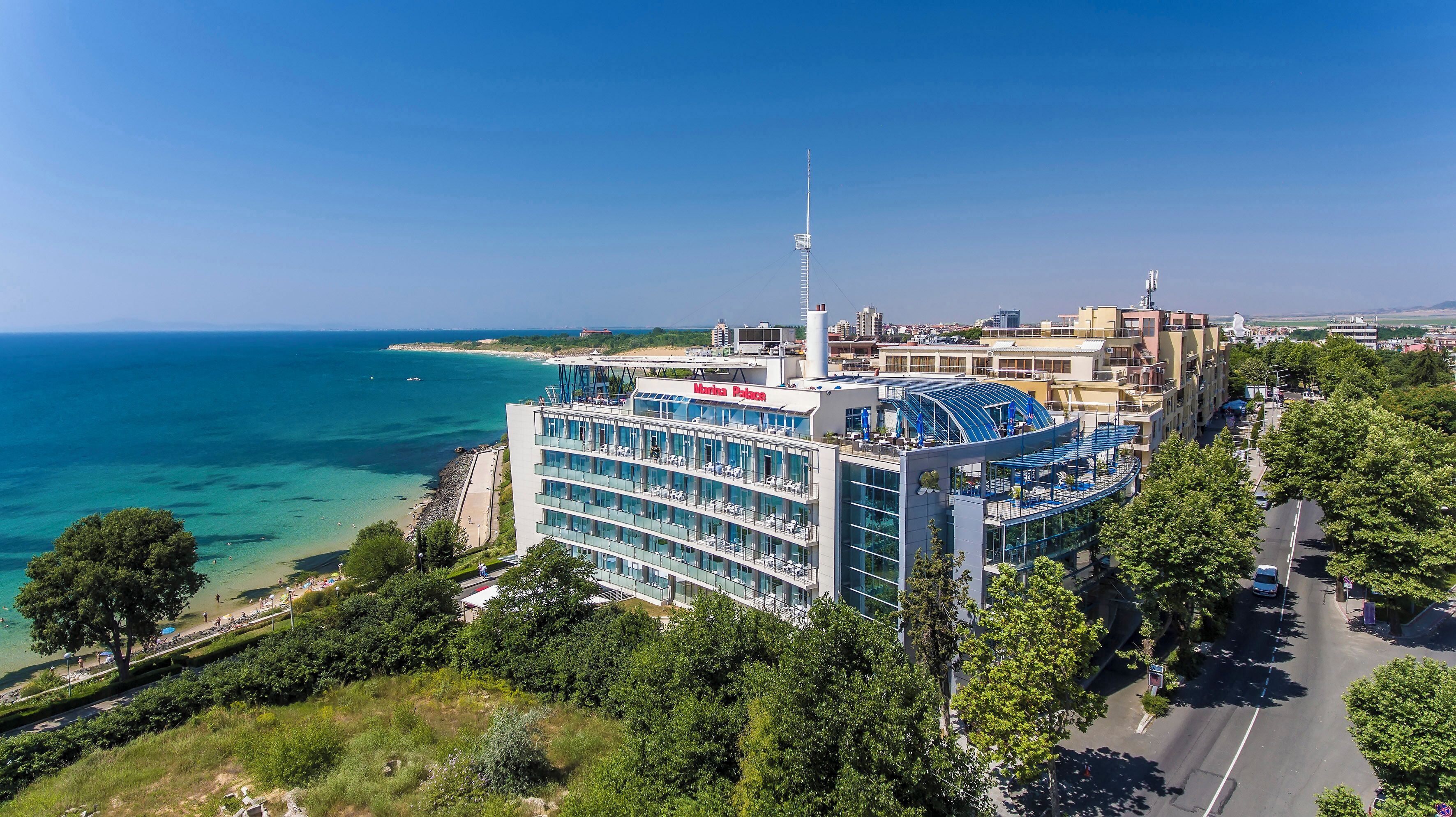A modern hotel with multiple floors, a prominent antenna, and a view of the sea.