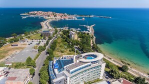 Vue aérienne d’une ville côtière avec un port de plaisance, un grand hôtel doté d’une piscine et, au loin, une ville historique.