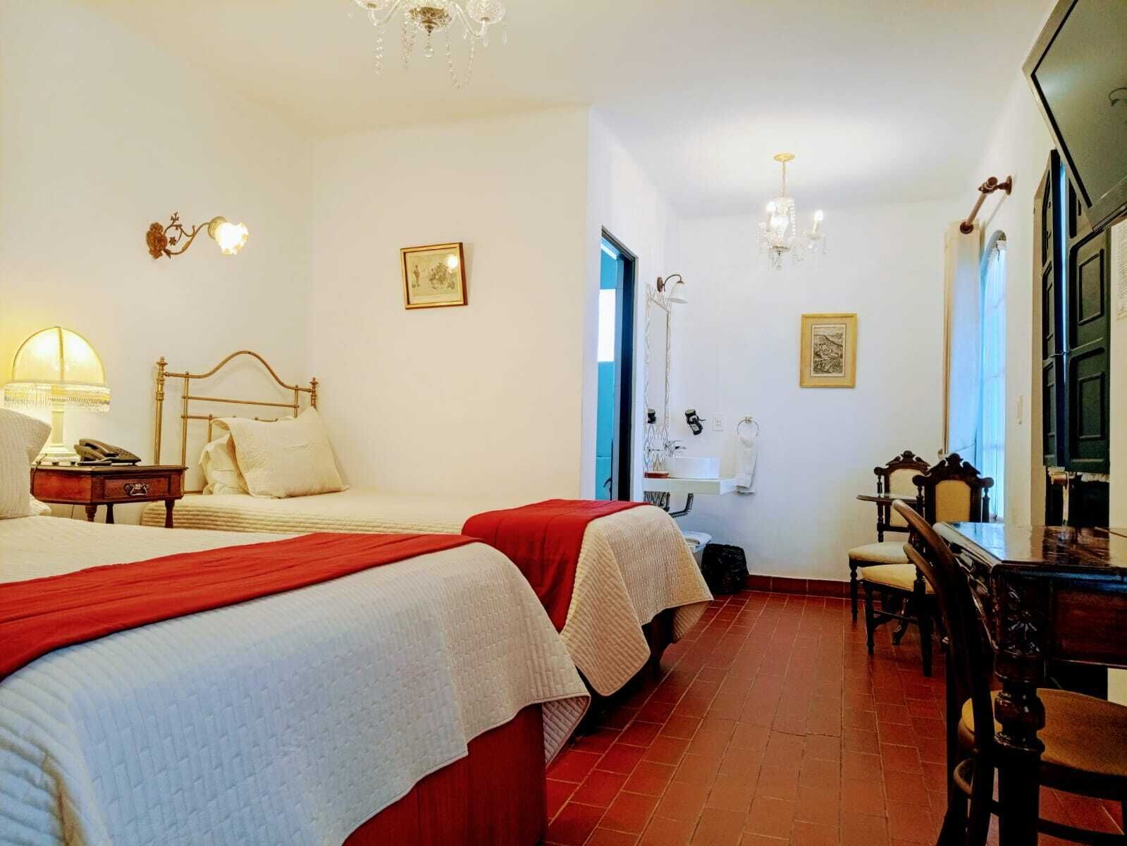 Een hotelkamer met twee bedden, een bureau, een stoel, een badkamer en een kroonluchter.