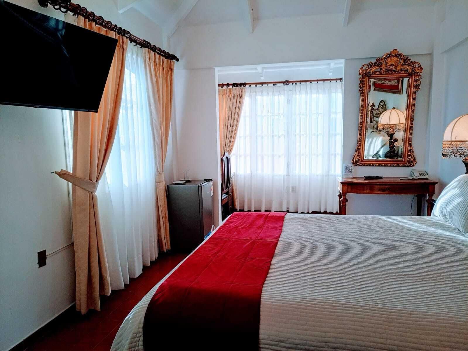 A hotel room with a bed, a television, a desk with a lamp, and a mirror.