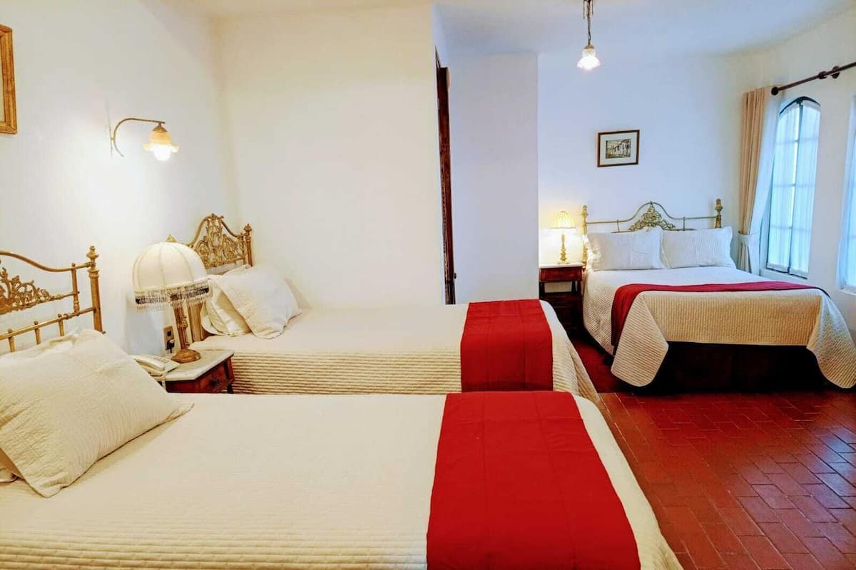 Quarto de hotel com duas camas, cabeceira de madeira, uma luminária e um quadro na parede.