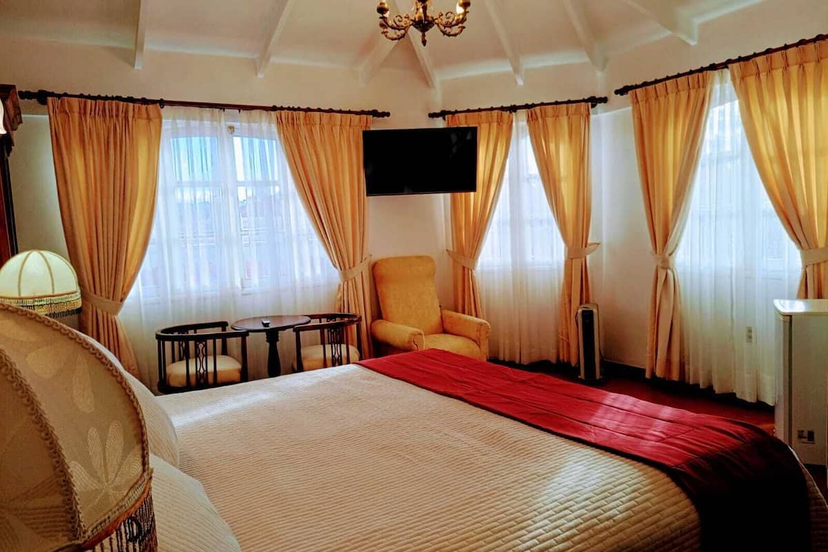 Quarto de hotel com cama, cadeira, mesa, televisão e cortinas.