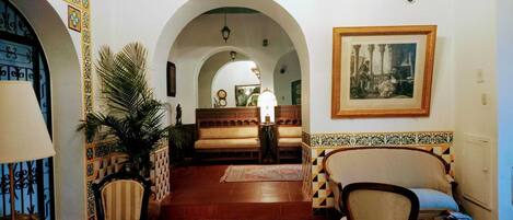A room with a sofa, chairs, a patterned rug, a lamp, a framed picture, and a plant.