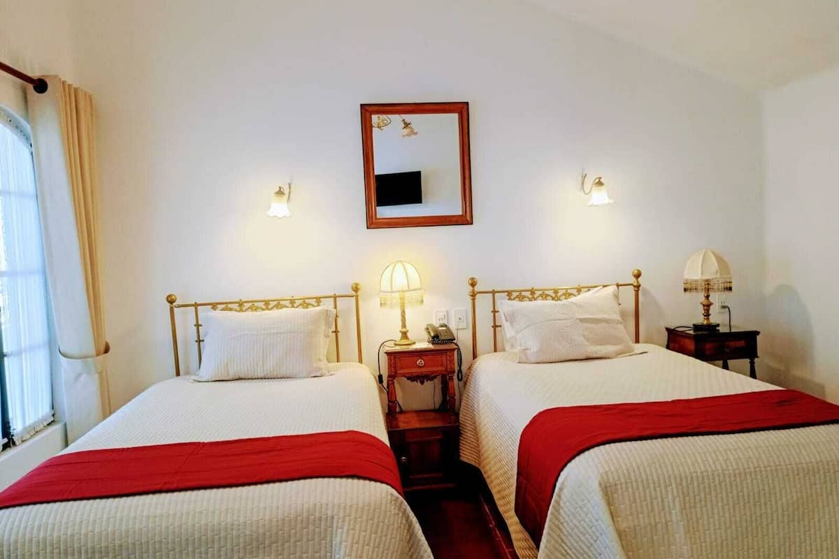 Quarto de hotel com duas camas, um espelho, abajures e uma janela com cortinas.