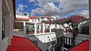 A courtyard with a white building, red-tiled roof, and a tree with pink flowers. - Hotel de Su Merced (Sucre)