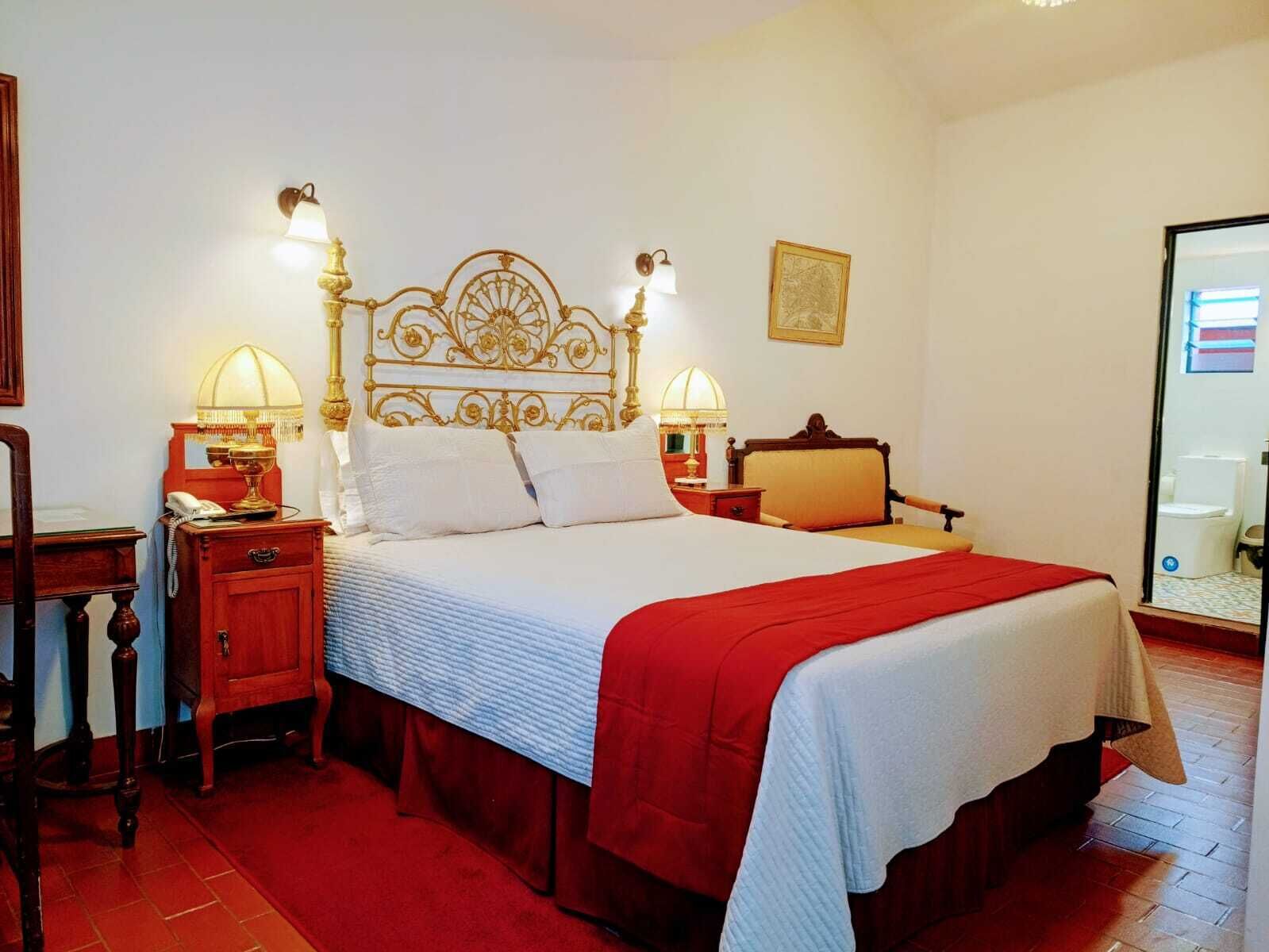 Ein Hotelzimmer mit einem großen Bett, zwei Nachttischen mit Lampen, einem Holznachttisch, einem roten Teppich und einem gerahmten Bild an der Wand.