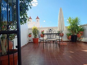 A terrace with a table and chairs, potted plants, and a view of a building with two towers. - Hotel de Su Merced (Sucre)