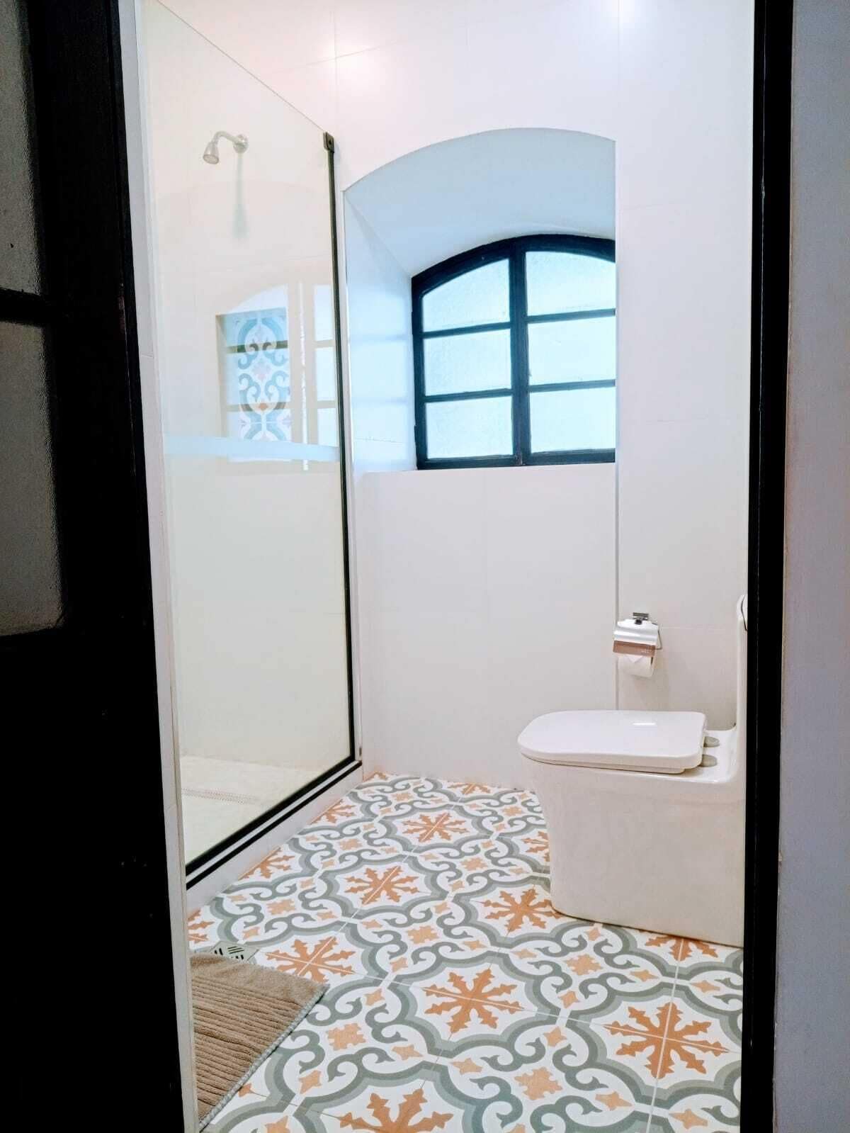 A bathroom with a shower, toilet, and patterned floor tiles.