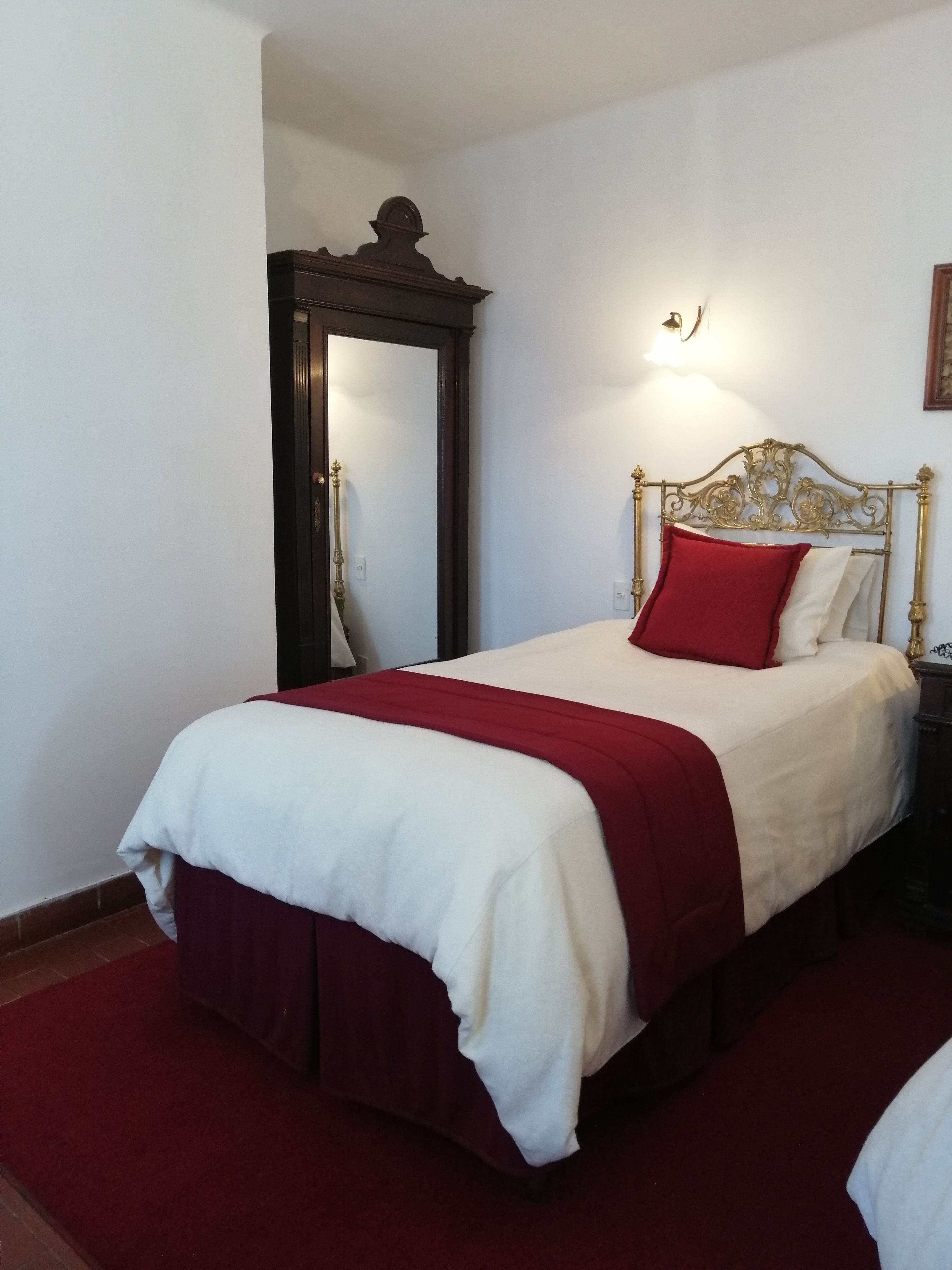 Un dormitorio con una cama, una mesita de noche, un espejo y una lámpara fijada a la pared.