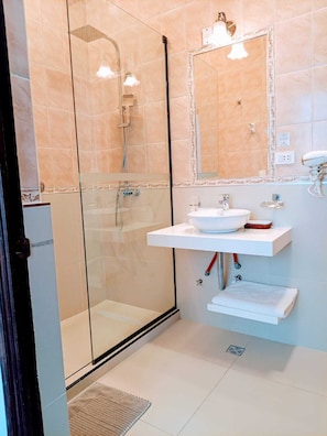 Un baño moderno con ducha de vidrio, lavamanos blanco y espejo con marco decorativo.