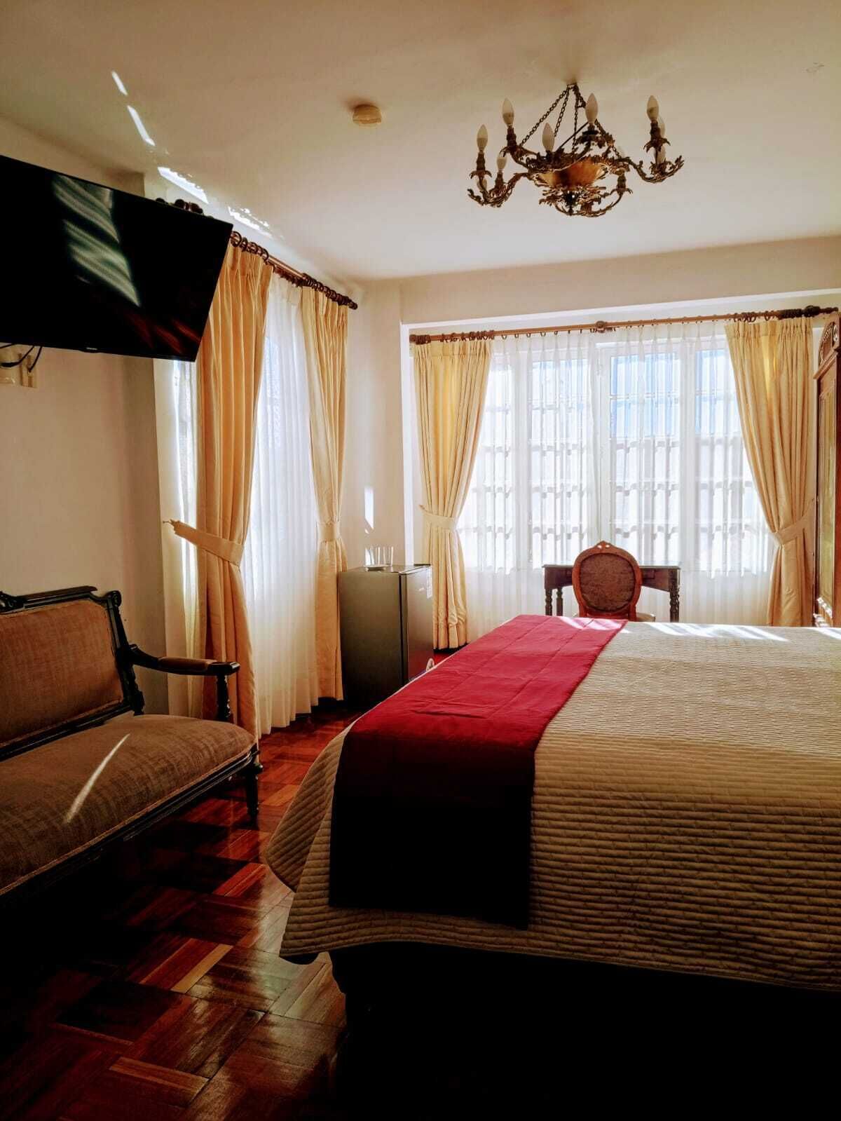 Una habitación de hotel con cama, una silla, televisor y candelabro.