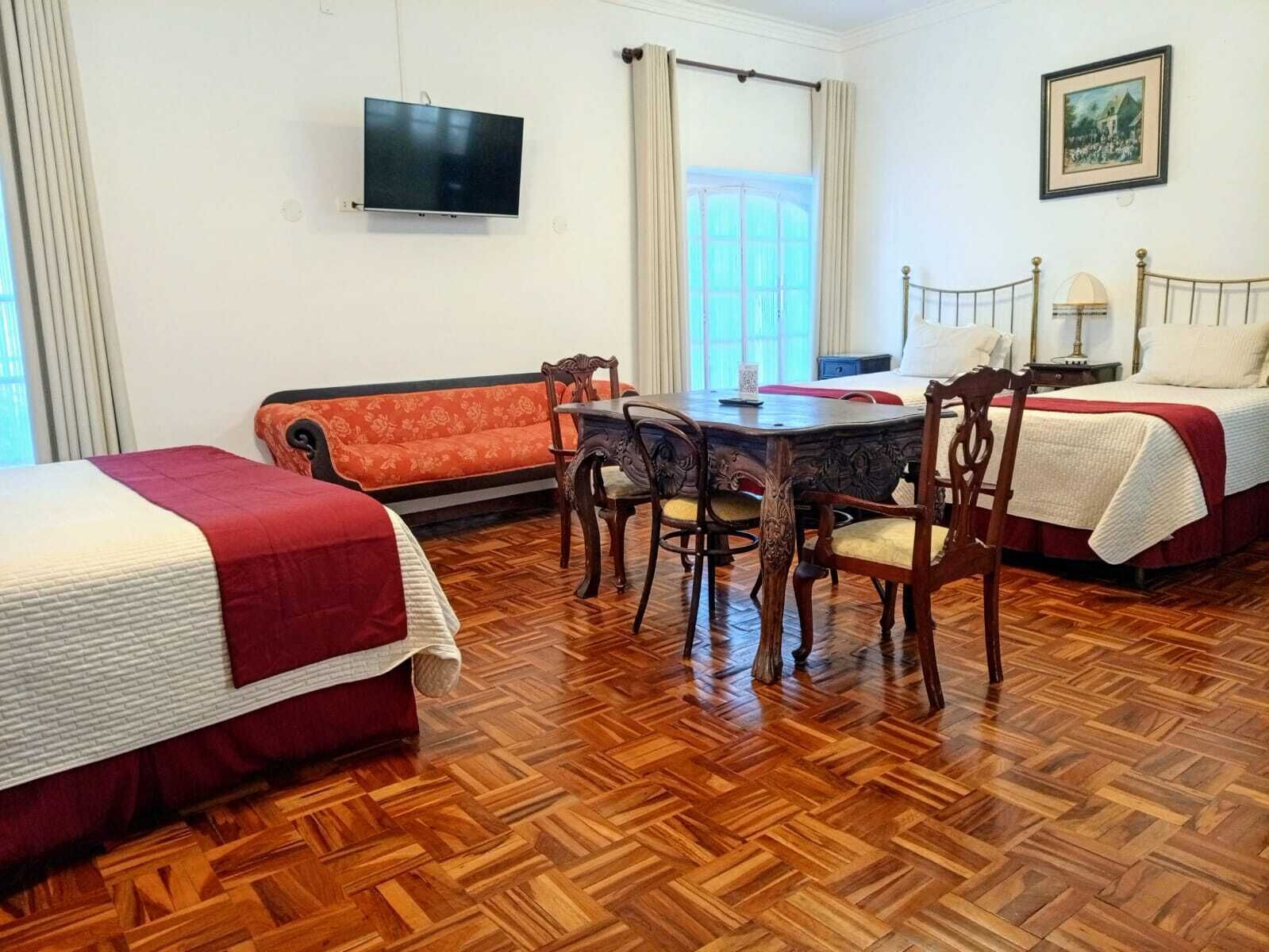 Habitación de hotel con dos camas, una mesa de comedor con sillas, un televisor y un cuadro en la pared.